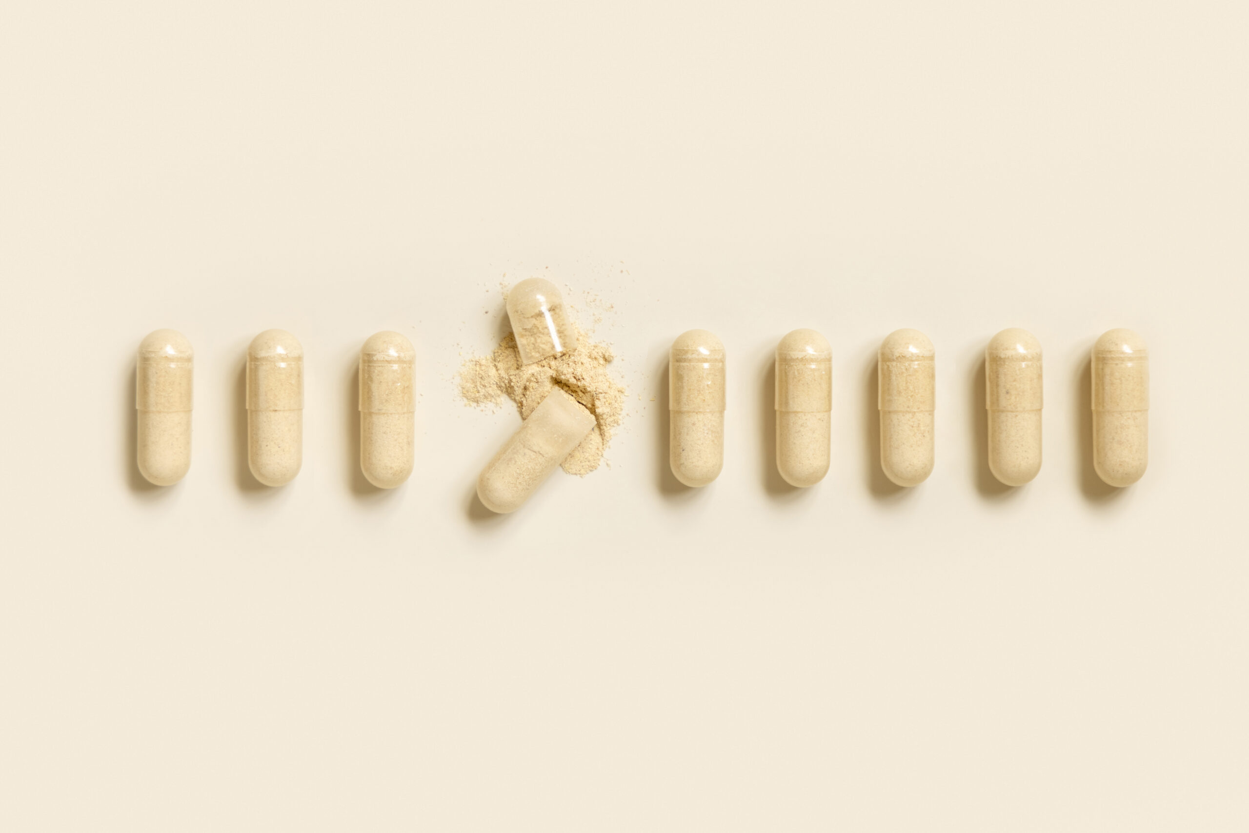 Supplement capsules lined up in a row on a beige background