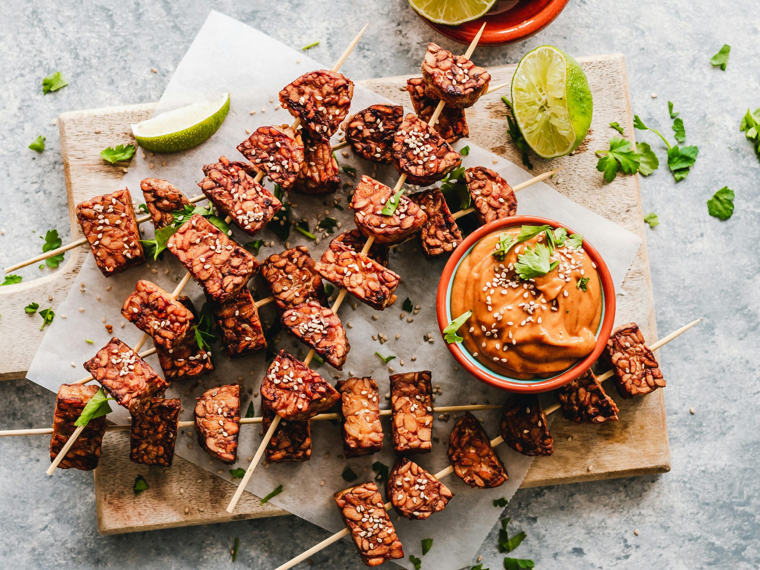 Tempe skewers with dip and garnishes on a wooden chopping board