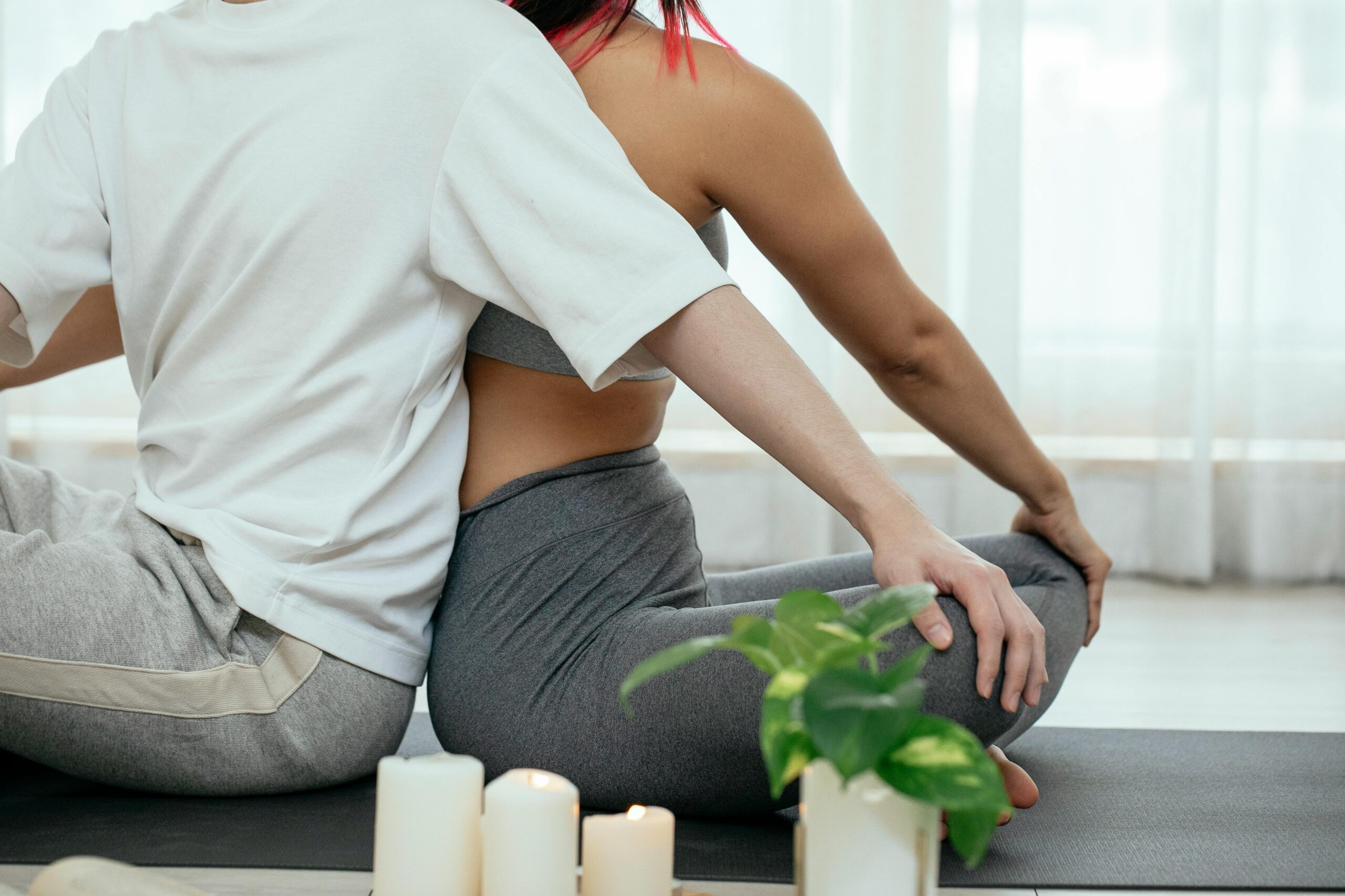 A man and a woman people sitting back to back doing yoga stretches