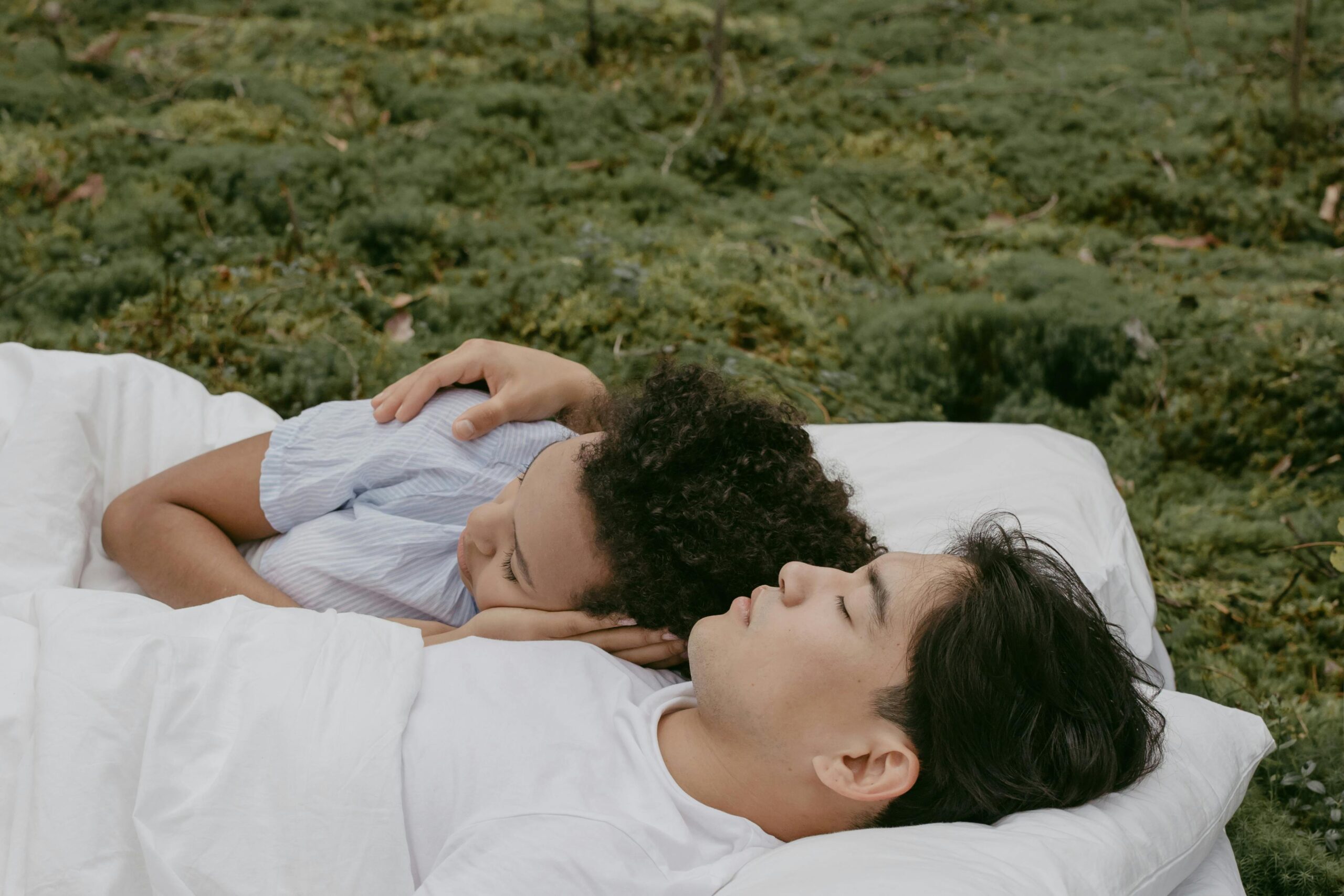 a couple of people lying on grass together cuddling