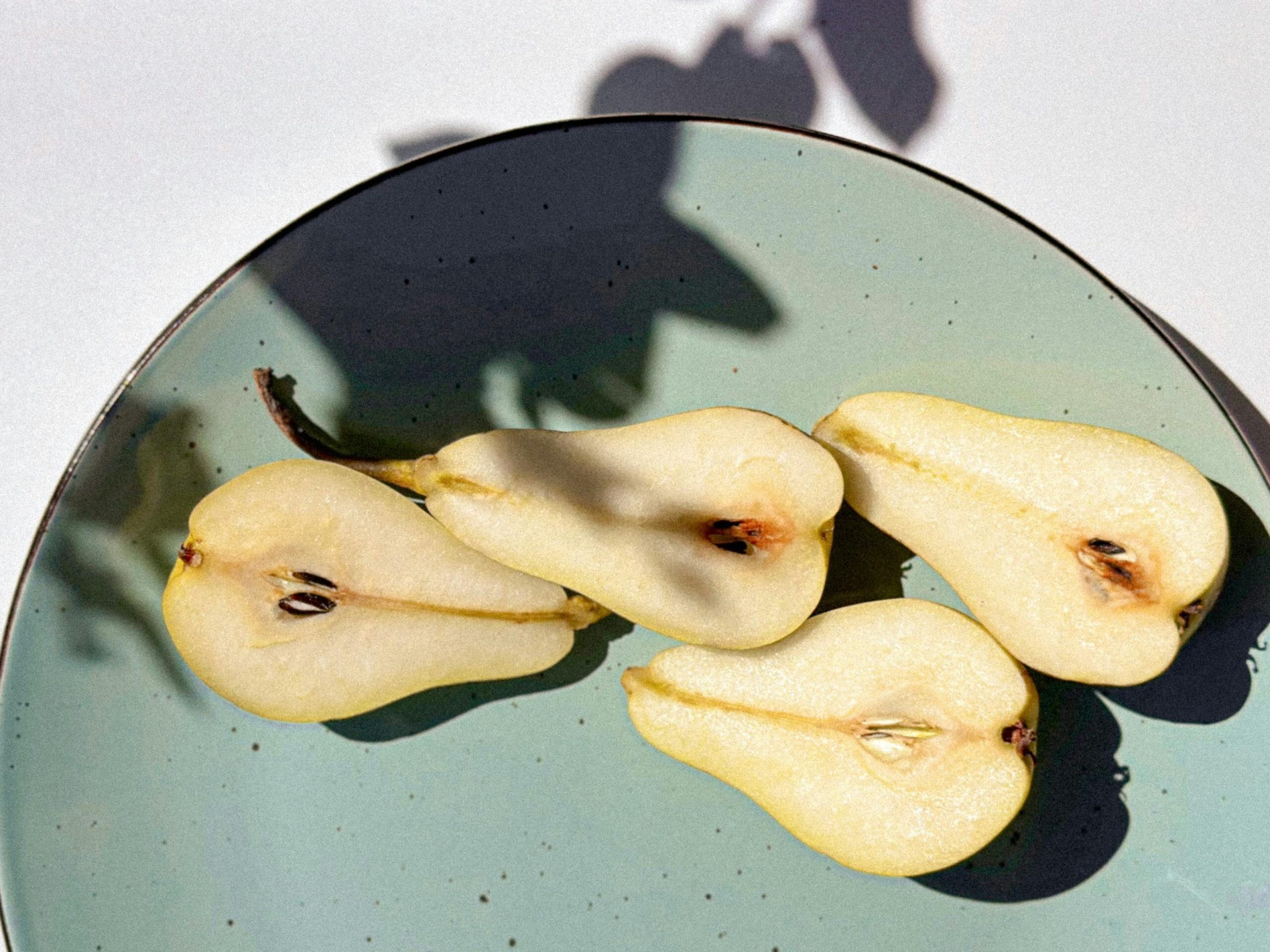 cut up pear on a blue plate with a white background and artistic shadow